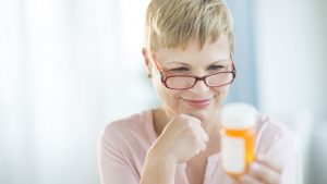 Woman with glasses reading the instructions on her pill bottle